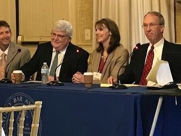 A panel of professionals sit behind a table with microphones and beverages.