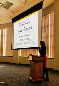 A woman is speaking at a podium in front of a projection screen